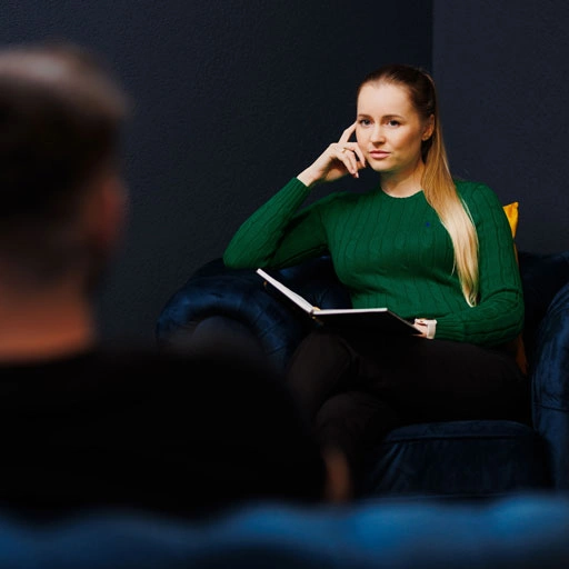 Psychoterapeutka w zielonym swetrze wysłuchuje klienta w trakcie psychoterapii